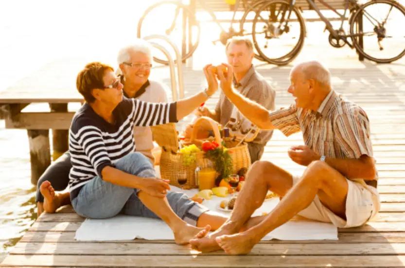 Retirees enjoy serene Mediterranean village life, laughing at a cafe with vibrant scenery around.