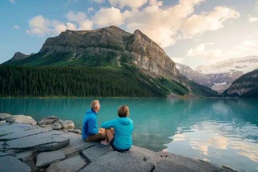 A serene lake surrounded by lush forests and mountains, with a bench and swans in view.