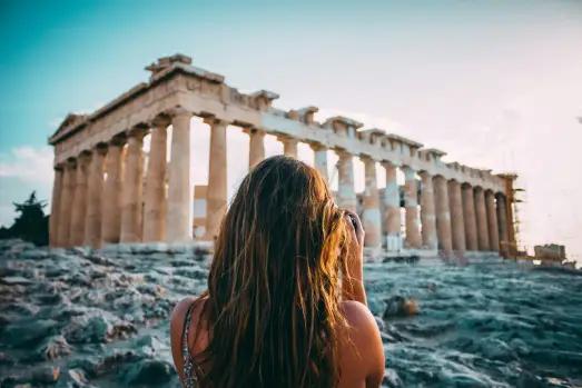 Elderly couple admiring the Parthenon's grandeur in Athens, Greece, against a sunlit backdrop.