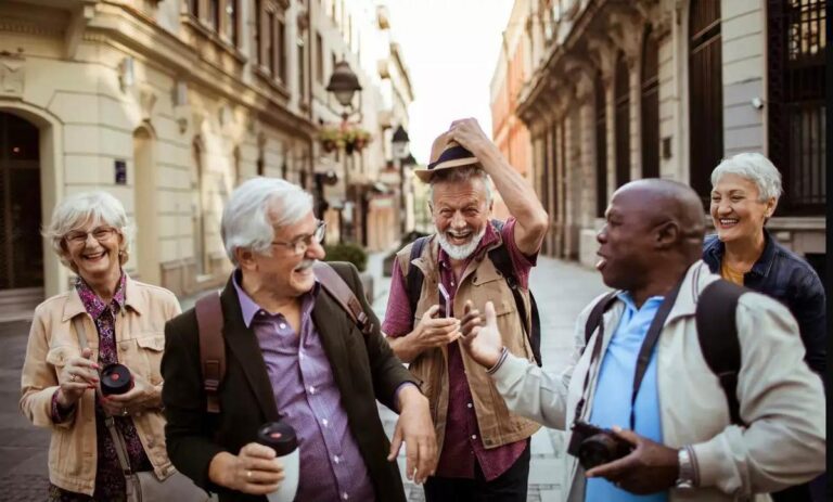 Cost of Living Comparison for Retirees Four retirees discussing finances on a lakeside deck at sunset, enjoying tea and laughter.