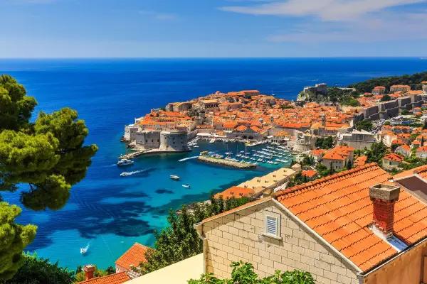 Retired couple enjoys wine and seafood on sunlit Croatian terrace overlooking the Adriatic Sea.