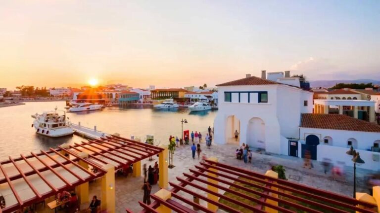 Alt Text: Retirees enjoying a bustling market square in a sunlit Cypriot village by the Mediterranean.