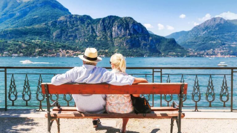 Retiree couple enjoying breakfast at an outdoor café in scenic Tuscany, surrounded by historic architecture.