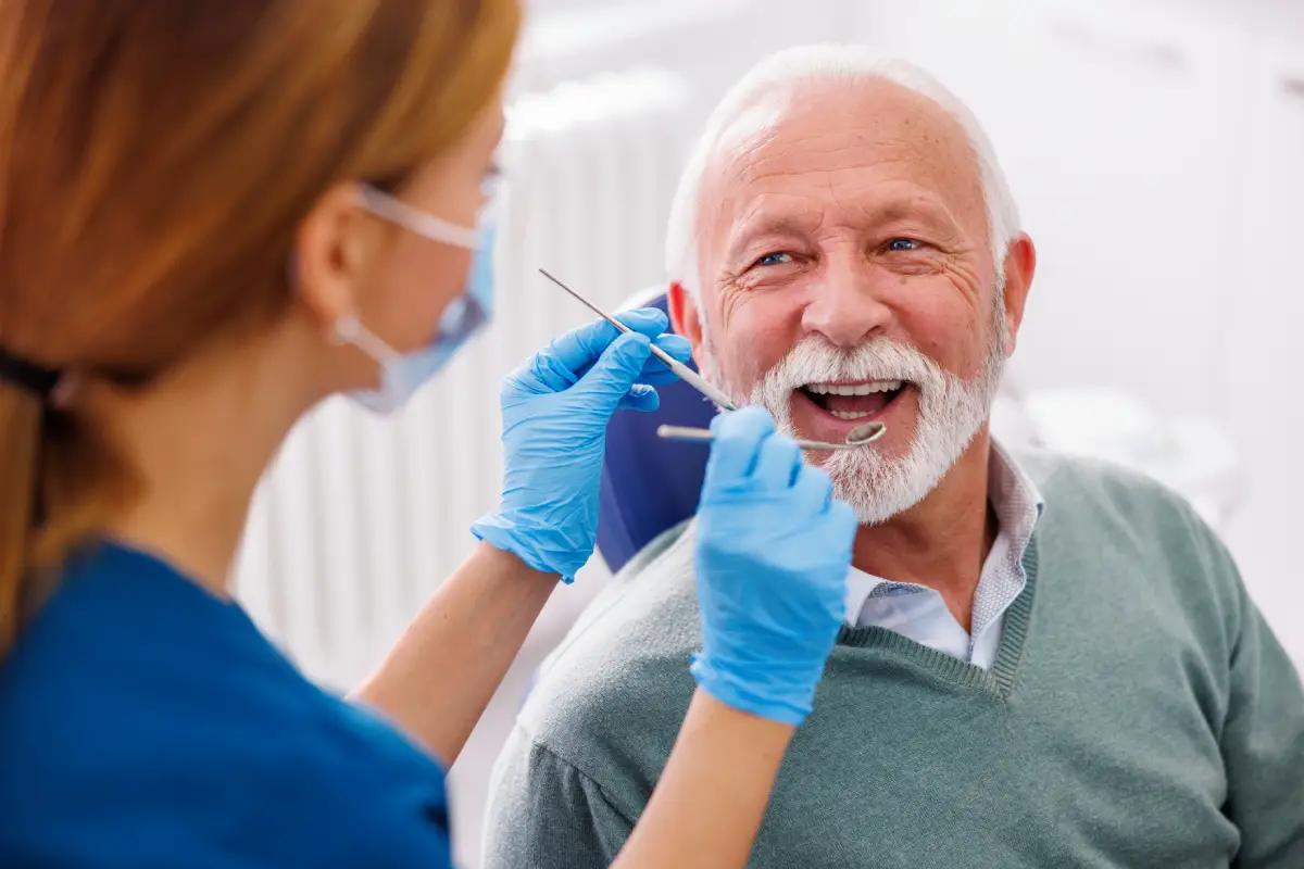 An elderly woman receives dental care while her husband reads a brochure, ocean view outside.