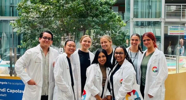 A retired couple strolls hand-in-hand through a serene, sunlit Italian village.